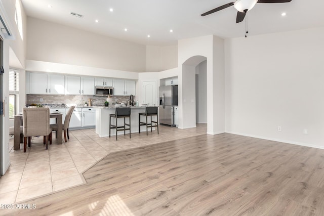 kitchen with an island with sink, ceiling fan, appliances with stainless steel finishes, a kitchen bar, and open floor plan