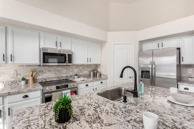 kitchen with light stone countertops, a sink, white cabinets, appliances with stainless steel finishes, and tasteful backsplash