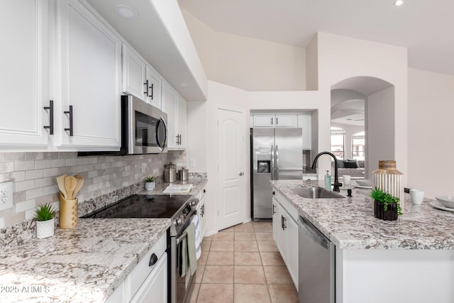 kitchen with backsplash, light stone countertops, appliances with stainless steel finishes, white cabinets, and a sink