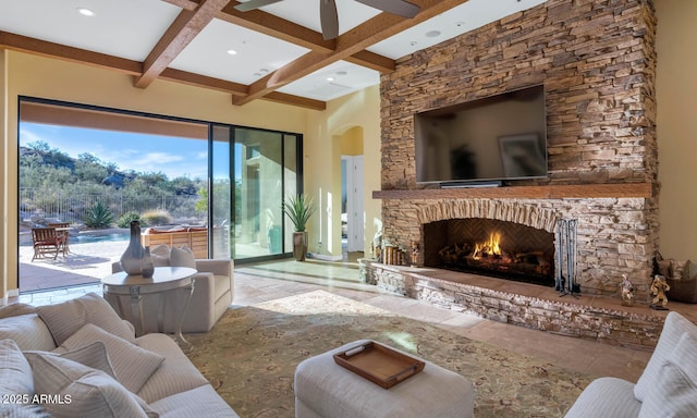 living room featuring ceiling fan, a stone fireplace, and beam ceiling