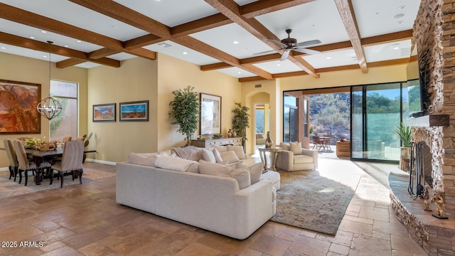 living room featuring a towering ceiling, ceiling fan with notable chandelier, a large fireplace, coffered ceiling, and beam ceiling