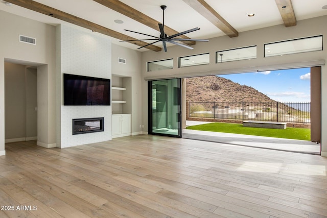 unfurnished living room with built in shelves, a towering ceiling, beam ceiling, and light hardwood / wood-style floors