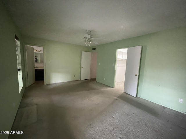 unfurnished bedroom featuring ceiling fan, a spacious closet, ensuite bath, and unfinished concrete floors