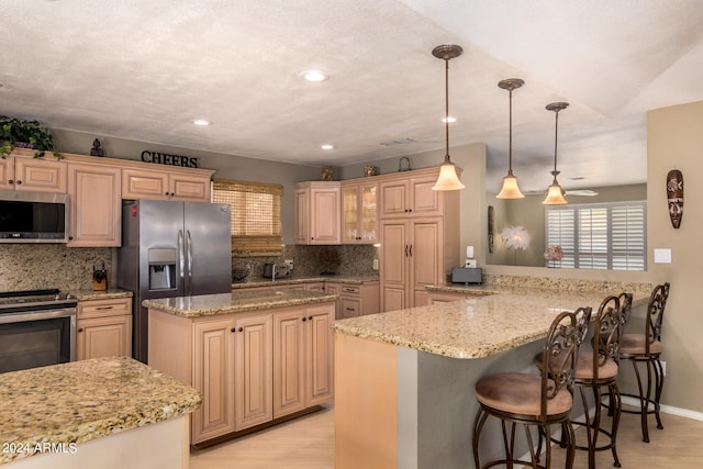 kitchen with light hardwood / wood-style floors, appliances with stainless steel finishes, kitchen peninsula, and backsplash