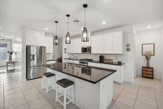 kitchen featuring appliances with stainless steel finishes, light tile patterned floors, a center island with sink, and white cabinetry