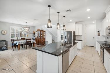 kitchen with white cabinets, an island with sink, stainless steel appliances, and decorative light fixtures