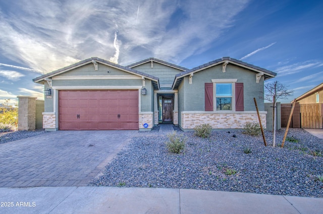 view of front of home with an attached garage, fence, stone siding, decorative driveway, and stucco siding