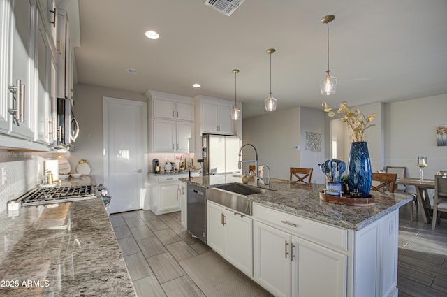 kitchen with stone counters, stainless steel appliances, visible vents, white cabinetry, and an island with sink