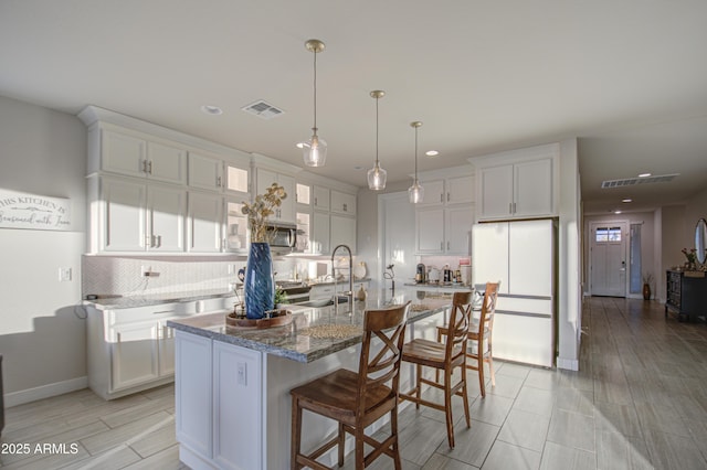 kitchen with freestanding refrigerator, white cabinets, a center island with sink, and visible vents