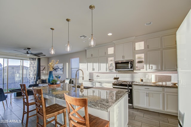 kitchen featuring a breakfast bar area, appliances with stainless steel finishes, light stone countertops, tasteful backsplash, and a center island with sink