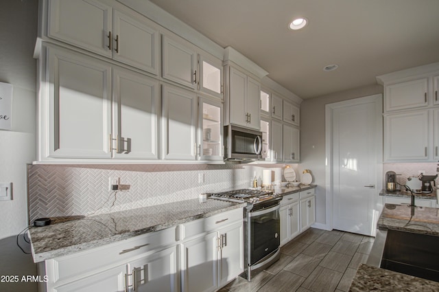 kitchen featuring light stone counters, stainless steel appliances, white cabinets, tasteful backsplash, and glass insert cabinets