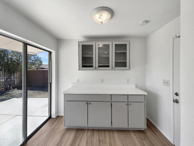 kitchen featuring glass insert cabinets, light countertops, gray cabinets, and light wood finished floors