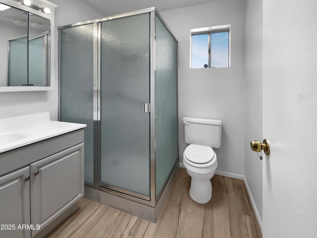 bathroom featuring toilet, wood finished floors, a shower stall, baseboards, and vanity