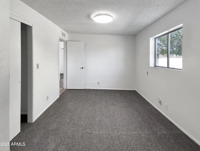 empty room with carpet flooring, a textured ceiling, baseboards, and visible vents