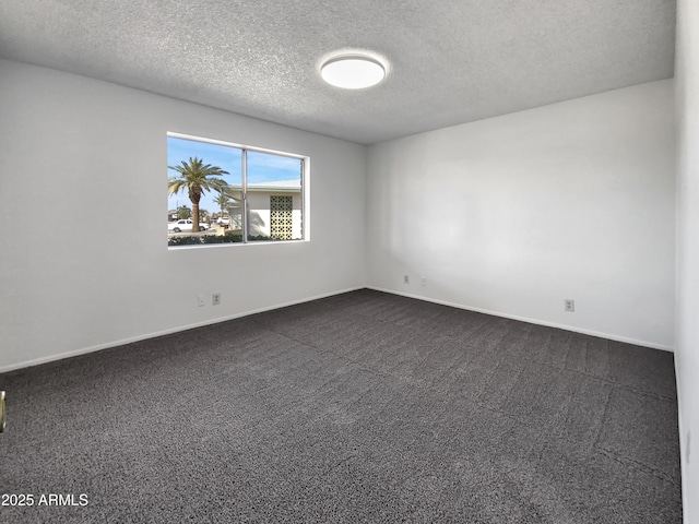 spare room featuring dark colored carpet, baseboards, and a textured ceiling