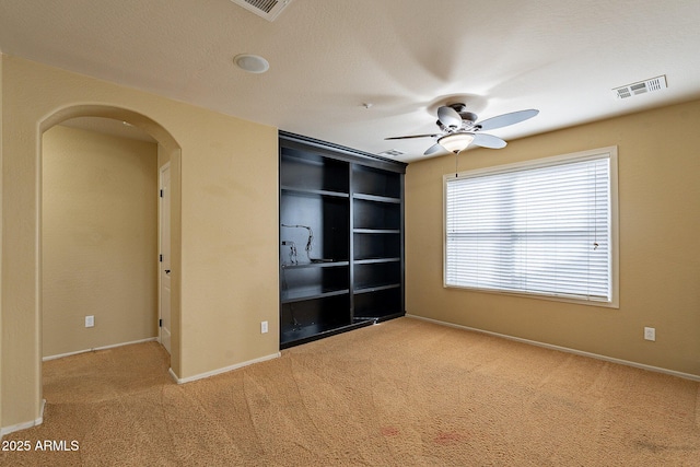 spare room with light colored carpet, built in features, and ceiling fan