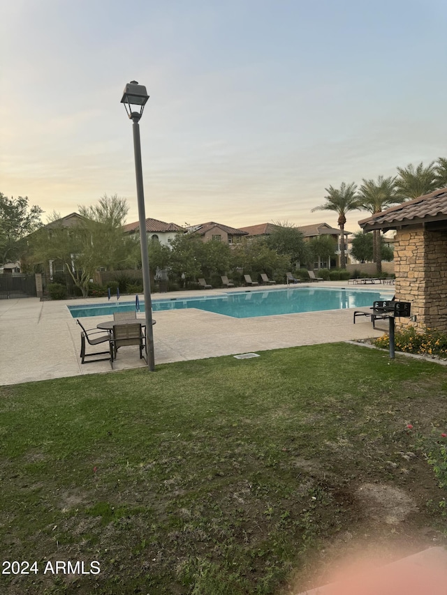 pool at dusk with a yard and a patio area