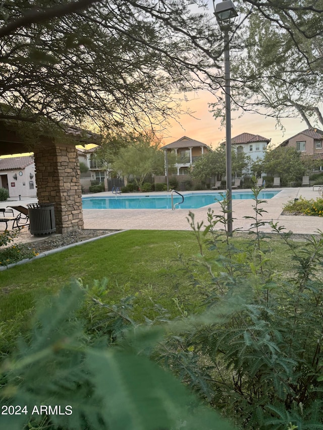 pool at dusk featuring a yard