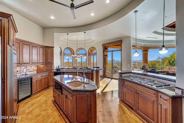 kitchen with tasteful backsplash, light hardwood / wood-style floors, wine cooler, a kitchen island with sink, and a tray ceiling