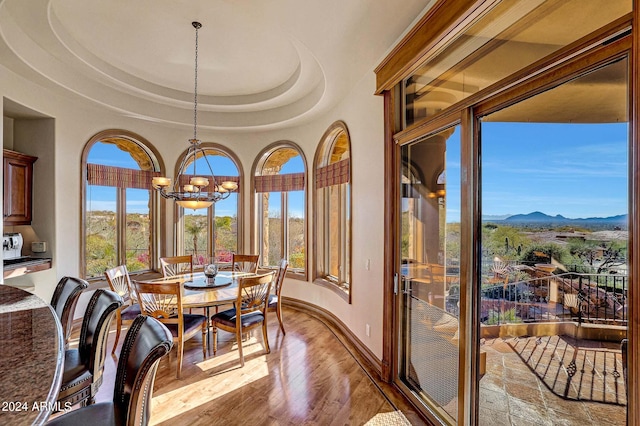 dining space featuring an inviting chandelier, a mountain view, a raised ceiling, and light hardwood / wood-style flooring