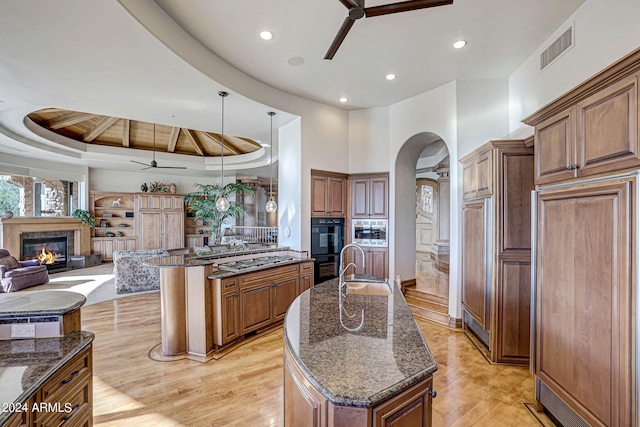 kitchen featuring an island with sink, ceiling fan, a towering ceiling, light hardwood / wood-style floors, and a tray ceiling