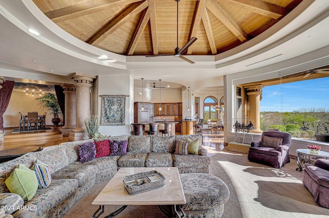 living room with beam ceiling, ceiling fan with notable chandelier, wooden ceiling, a high ceiling, and ornate columns