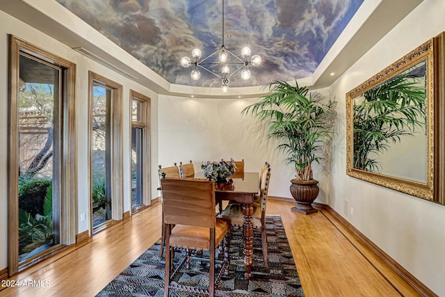 dining space featuring a raised ceiling, light wood-type flooring, and an inviting chandelier