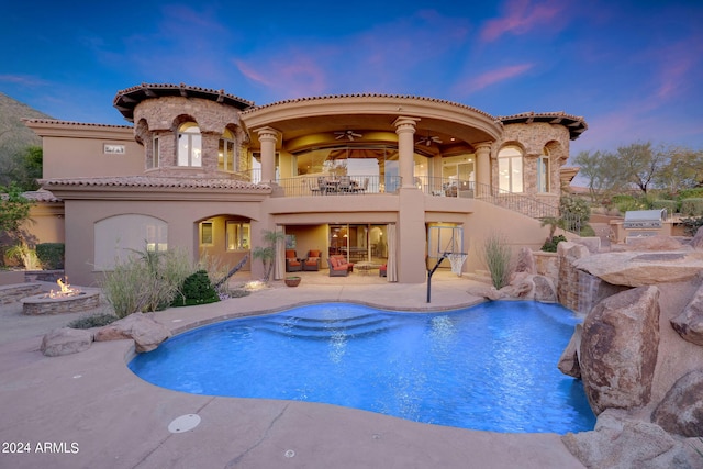 back house at dusk with a fire pit, pool water feature, a balcony, and a patio