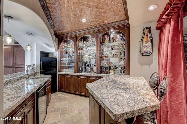 bar featuring wine cooler, decorative light fixtures, light stone counters, and black fridge