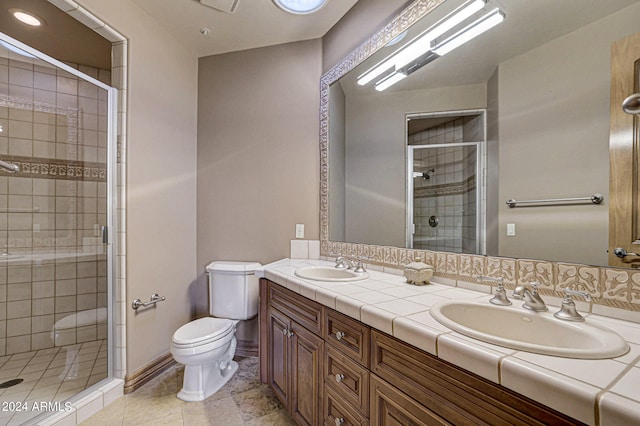 bathroom with dual sinks, a shower with door, tile flooring, vanity with extensive cabinet space, and toilet