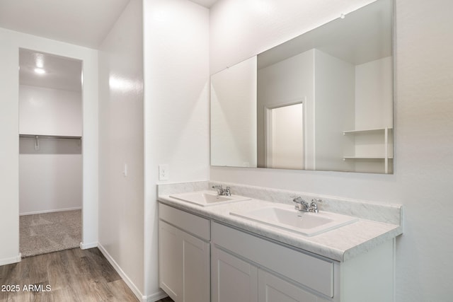 bathroom with a sink, baseboards, double vanity, and wood finished floors