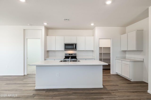 kitchen with a kitchen island with sink, visible vents, light countertops, dark wood-style floors, and stainless steel appliances