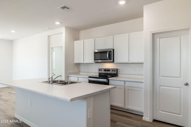 kitchen featuring visible vents, a sink, dark wood-style floors, stainless steel appliances, and an island with sink