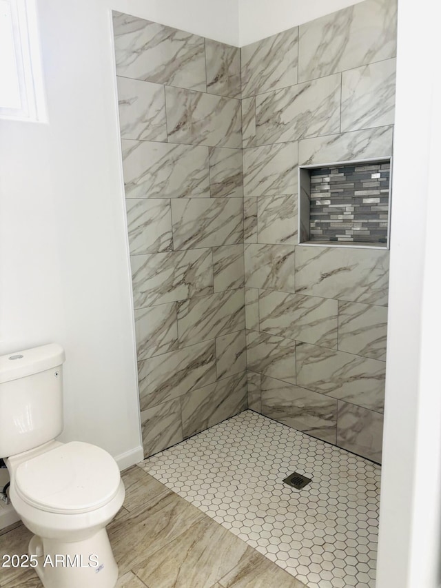 bathroom featuring toilet, baseboards, and tiled shower