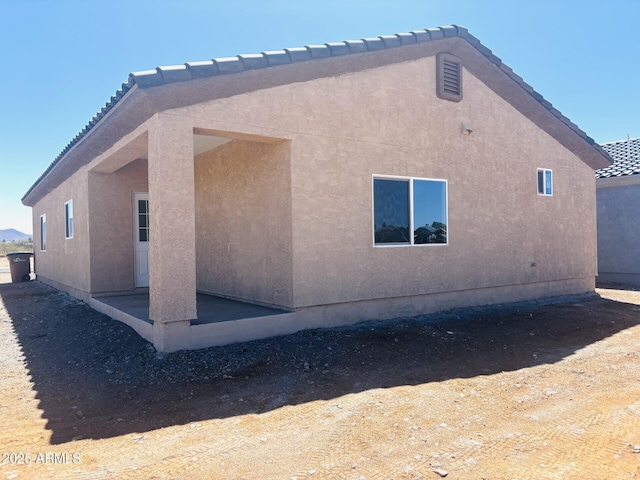 view of home's exterior with stucco siding, a tiled roof, and a patio