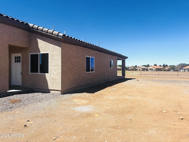 view of home's exterior featuring fence, a tiled roof, and stucco siding
