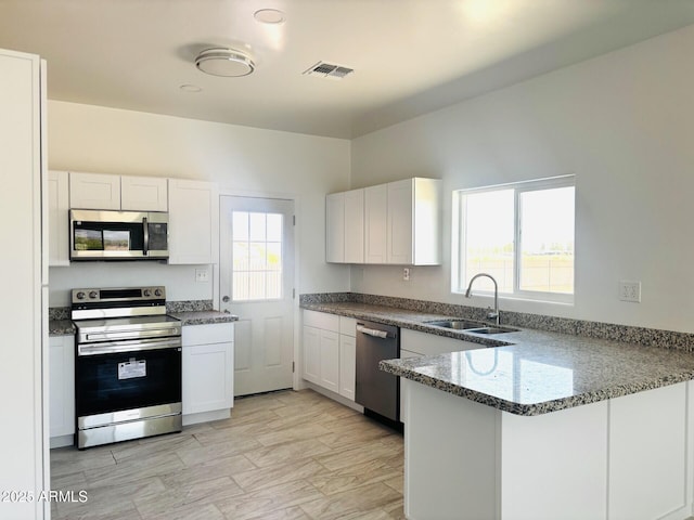 kitchen with white cabinets, stainless steel appliances, a peninsula, and a sink