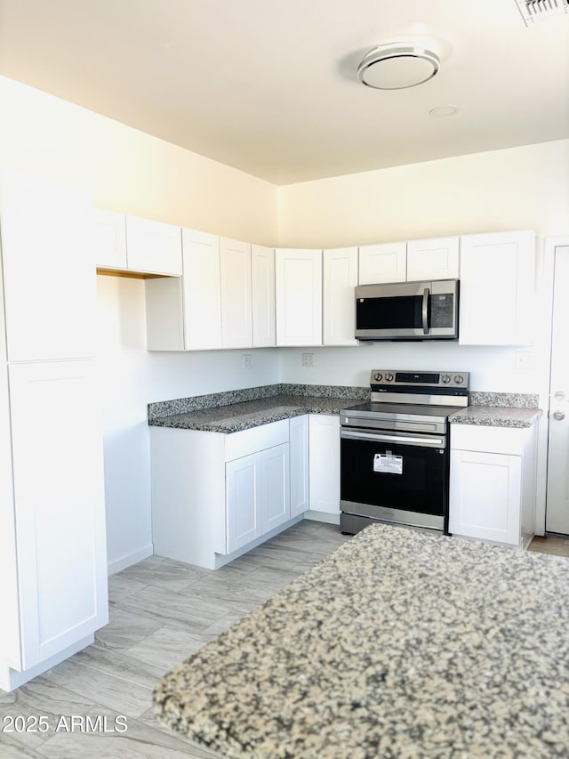 kitchen featuring light stone counters, appliances with stainless steel finishes, baseboards, and white cabinetry