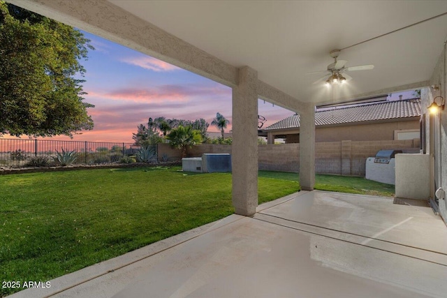 patio terrace at dusk featuring exterior kitchen, a yard, and ceiling fan