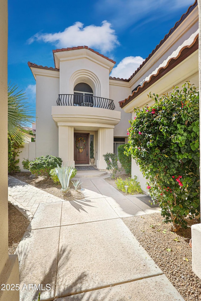 doorway to property featuring a tiled roof, a balcony, and stucco siding