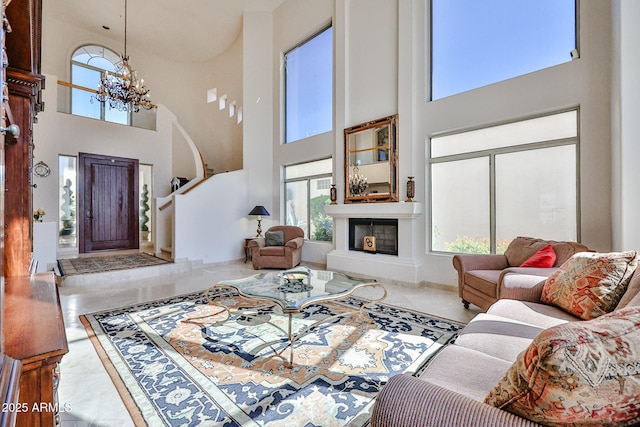 living room with tile patterned flooring, a glass covered fireplace, a towering ceiling, and a notable chandelier