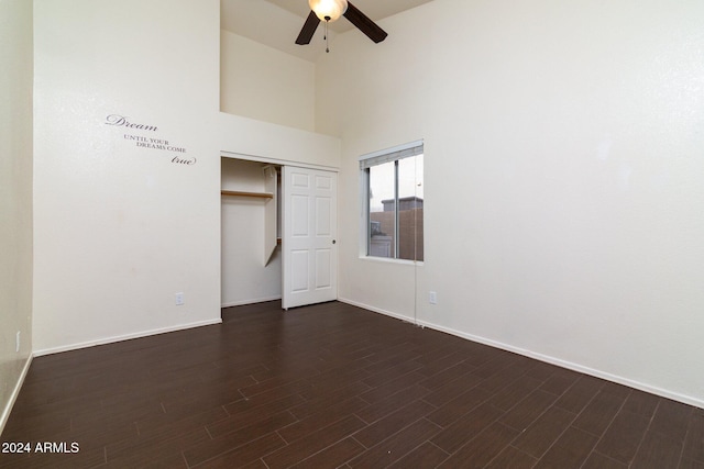 unfurnished bedroom featuring a closet, ceiling fan, dark hardwood / wood-style flooring, and a towering ceiling