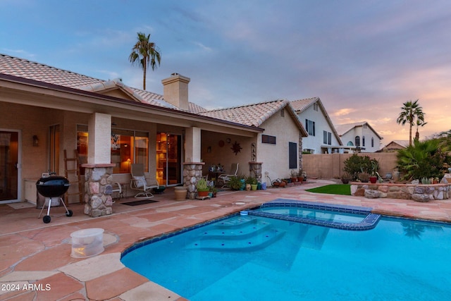 pool at dusk with a grill, an in ground hot tub, and a patio