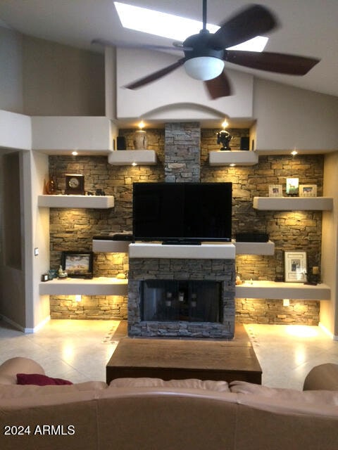 living room with ceiling fan, a stone fireplace, and vaulted ceiling