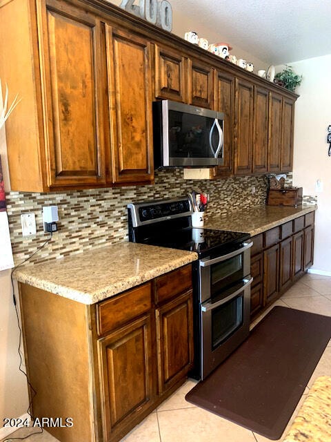 kitchen with decorative backsplash, light tile patterned floors, stainless steel appliances, and light stone countertops