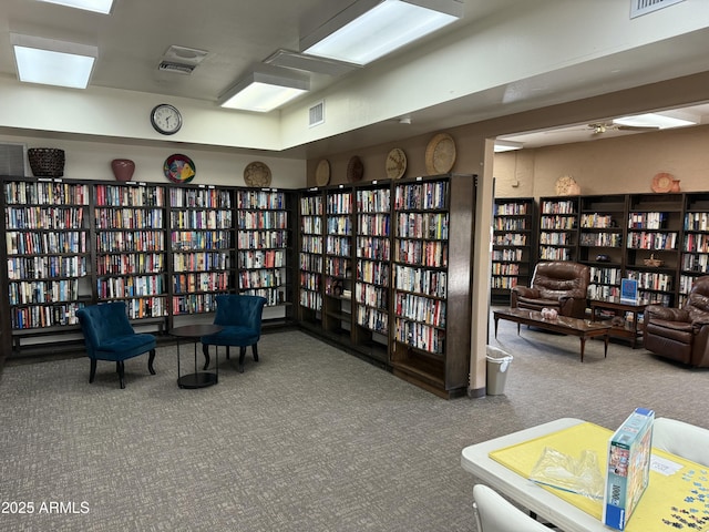 living area with bookshelves, carpet flooring, and visible vents