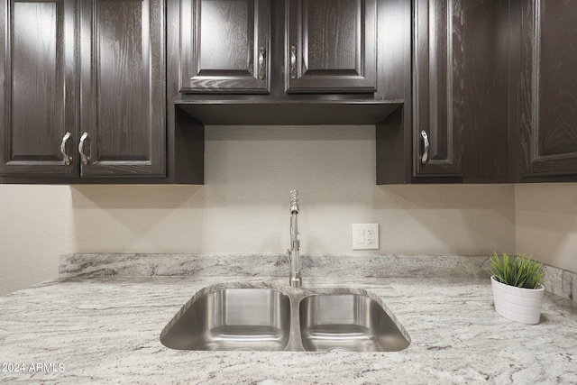 kitchen featuring dark brown cabinetry, sink, and light stone countertops