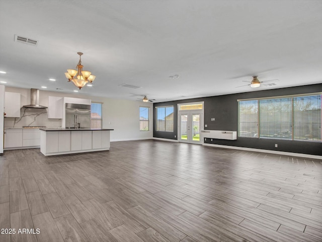 unfurnished living room with ceiling fan with notable chandelier, visible vents, and wood finished floors