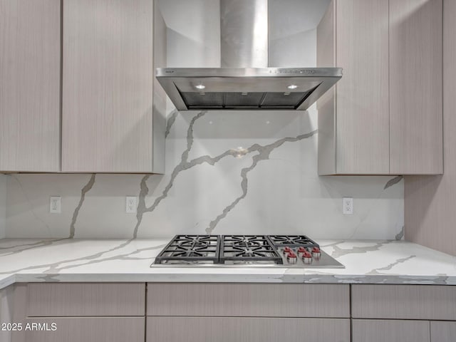 kitchen featuring light brown cabinets, stainless steel gas stovetop, wall chimney exhaust hood, and light stone countertops