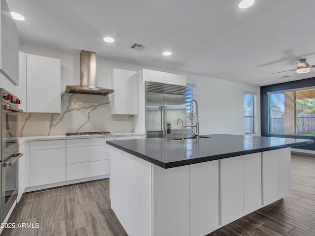 kitchen with visible vents, white cabinetry, wall chimney range hood, appliances with stainless steel finishes, and light wood-type flooring